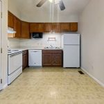 Apartment kitchen with wood cabinets, white appliances, and open floor space at Emerald Pointe Senior Living.