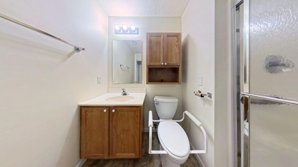 Apartment 204 bathroom with wood vanity, toilet support rails, and shower at Emerald Pointe Senior Living.