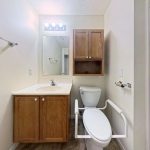 Apartment 204 bathroom with wood vanity, toilet support rails, and shower at Emerald Pointe Senior Living.