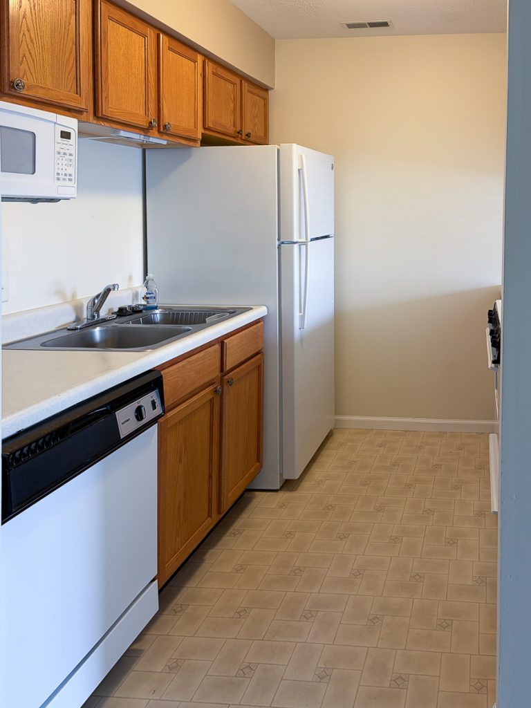 Apartment 204 kitchen with wood cabinets, sink, dishwasher, and refrigerator at Emerald Pointe Senior Living.