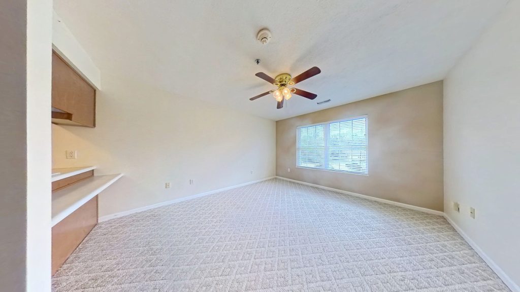 Unfurnished apartment 204 living room with carpet, window, and ceiling fan at Emerald Pointe Senior Living.